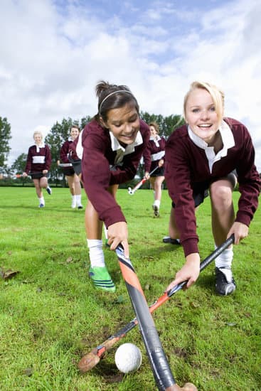 Girls playing a field hockey game in full uniform with shin guards and field hockey sticks hitting a ball on the pitch